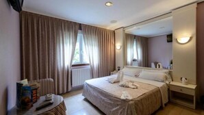 Hotelkamer met een groot bed, nachtkastje met lamp, spiegel en raam met gordijnen.