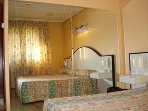 Een hotelkamer met twee bedden, een nachtkastje, een spiegel en een klein bureau met een lamp.