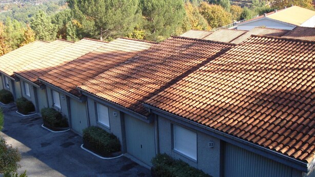 A row of motel buildings with a tiled roof, numbered parking spaces, and a view of a hilly landscape. - Motel Cancun Barbadas Ourense (Barbadas)