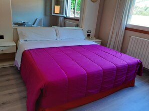 Ein Bett mit einer hellrosa Bettdecke, ein Nachttisch und ein Nachtschränkchen.