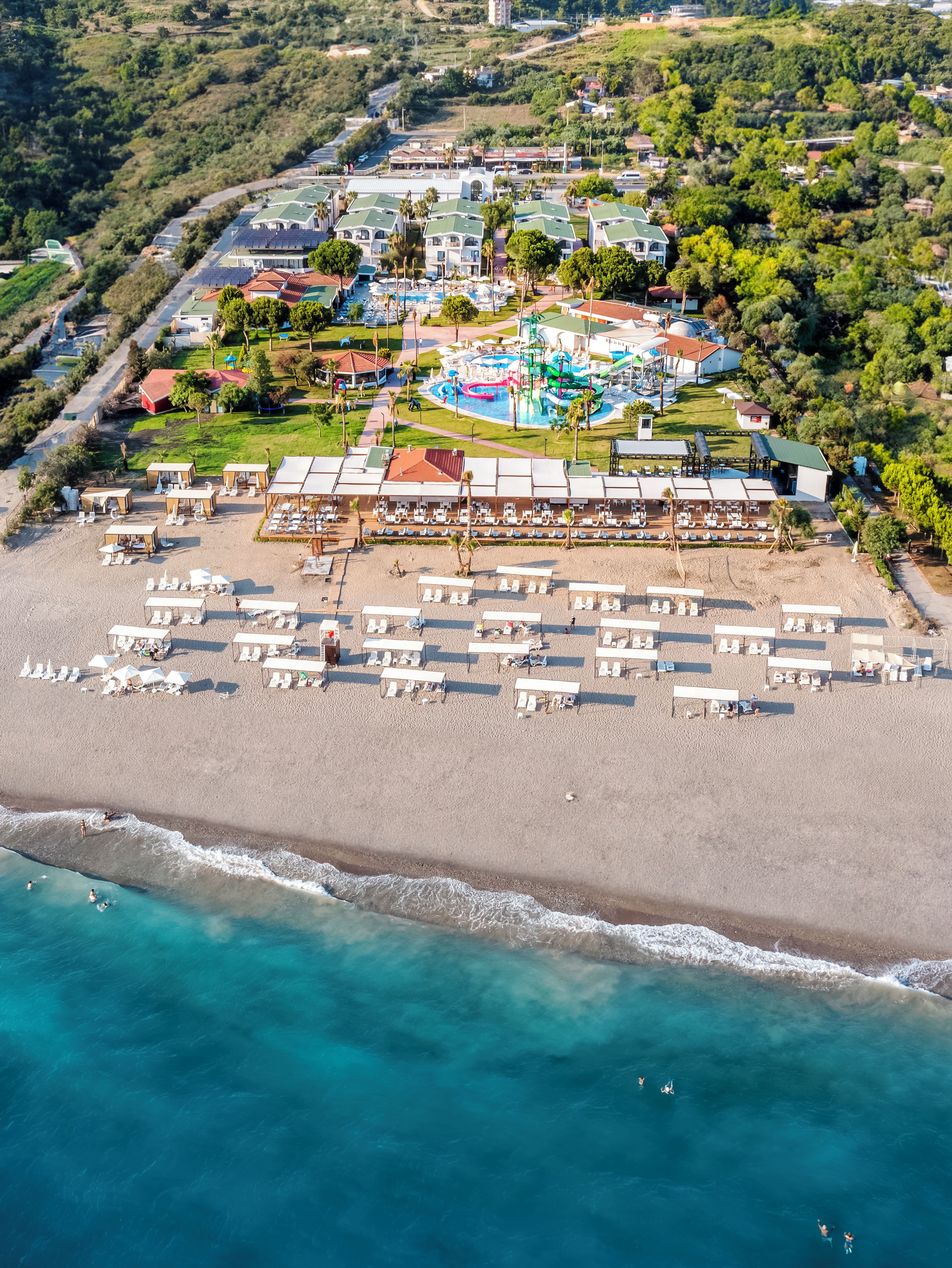 An aerial view of a coastal resort with a beach, pool area, and multiple buildings.