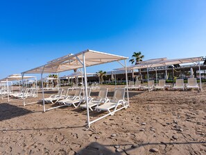 Een strand met ligbedden onder parasols, palmbomen en een heldere lucht.