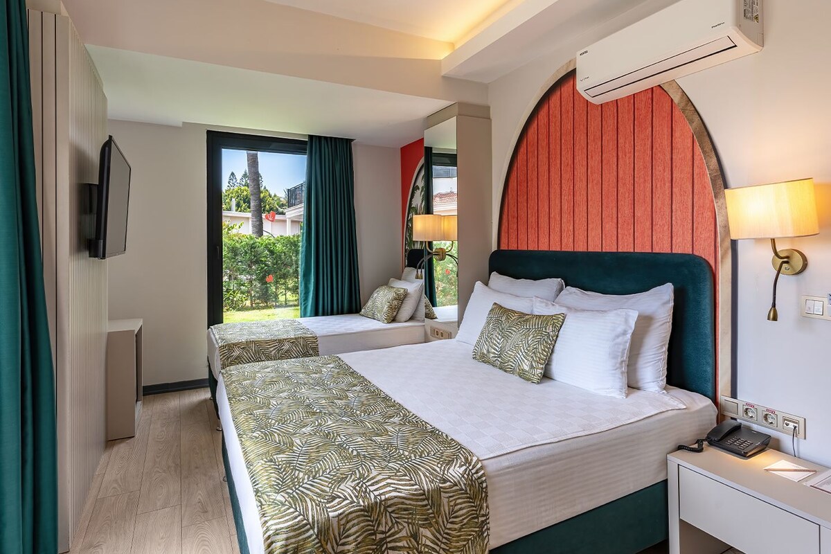 Ein Hotelzimmer mit Bett, Nachttisch, Lampe, Klimaanlage und Blick ins Freie.