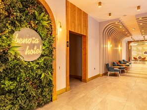 A hotel reception area with a neon sign, a plant wall, and a seating area with chairs. - La Benata Beach Hotel (Manavgat)
