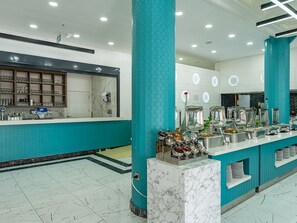 Een moderne buffetruimte met een marmeren aanrecht, kolommen in teal-kleur, en diverse voedselcontainers.