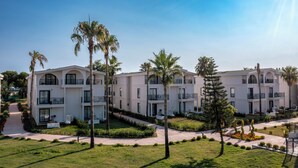 Un hotel de varios pisos con balcones, un césped cuidado y palmeras.