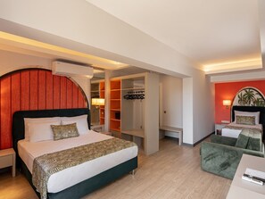 Ein Hotelzimmer mit einem Bett, einem Schreibtisch, einem grünen Sessel, einem Kleiderschrank und einer roten Wand.