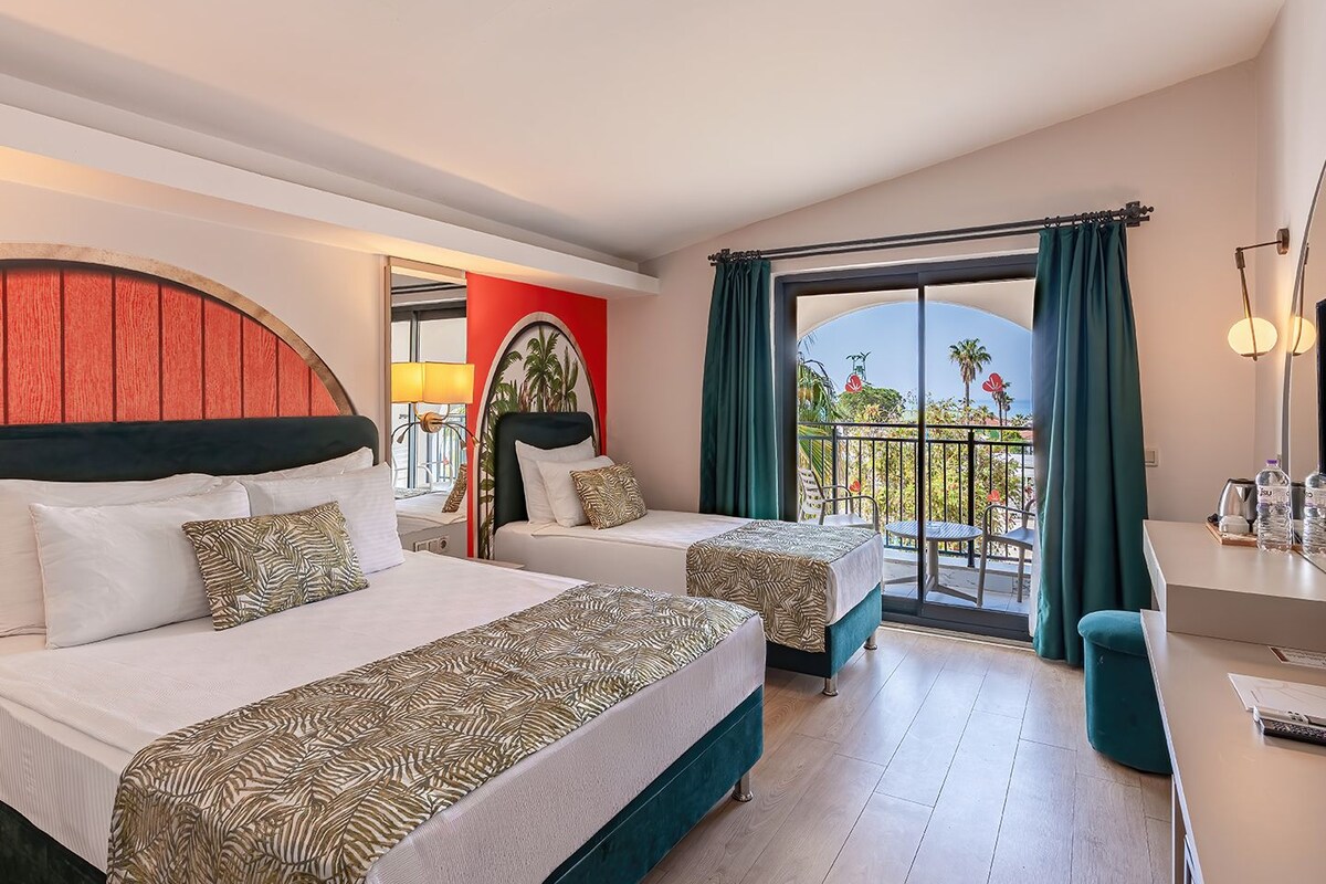 Ein Hotelzimmer mit zwei Betten, einem Balkon mit Blick und einem Schreibtisch mit Lampe.