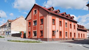 Un edificio rosso con la segnaletica 'HOTEL KÁCOV', vista dalla strada, e cielo sereno.