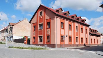 A red building with 'HOTEL KÁCOV' signage, a street view, and a clear sky.