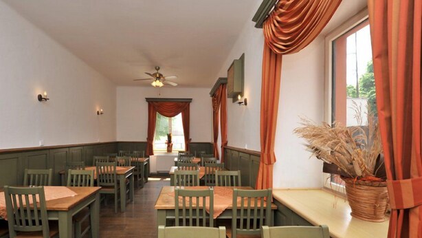 Un ristorante con tavoli e sedie di legno, una ventola a soffitto e una finestra con tende.