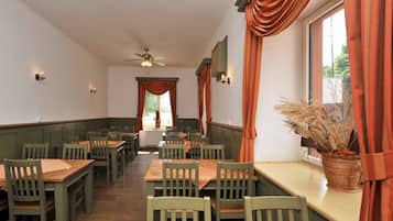 A restaurant with wooden tables and chairs, a ceiling fan, and a window with curtains.