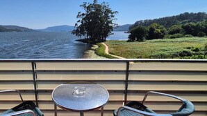 Un balcón con una mesa y dos sillas, con vista a un lago, un árbol y colinas a lo lejos.