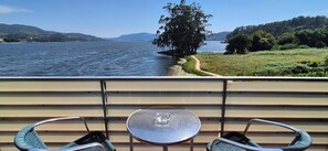 Un balcón con una mesa y dos sillas, con vista a un lago, un árbol y colinas a lo lejos.