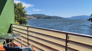 Un balcón con vista a un lago y colinas distantes, amueblado con dos sillas y una mesa.