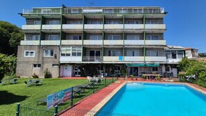 A multi-story hotel with a swimming pool, outdoor seating, and a green lawn. - Las Islas (Vilaboa)