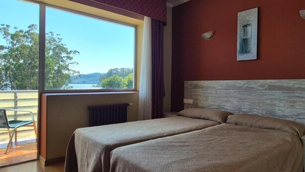 A hotel room with two beds, a view of the outdoors, and a window with curtains. - Las Islas (Vilaboa)
