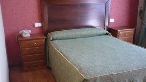 A bedroom with a wooden headboard, a green bedspread, a wooden nightstand with a telephone, and a wooden dresser. - Las Islas (Vilaboa)