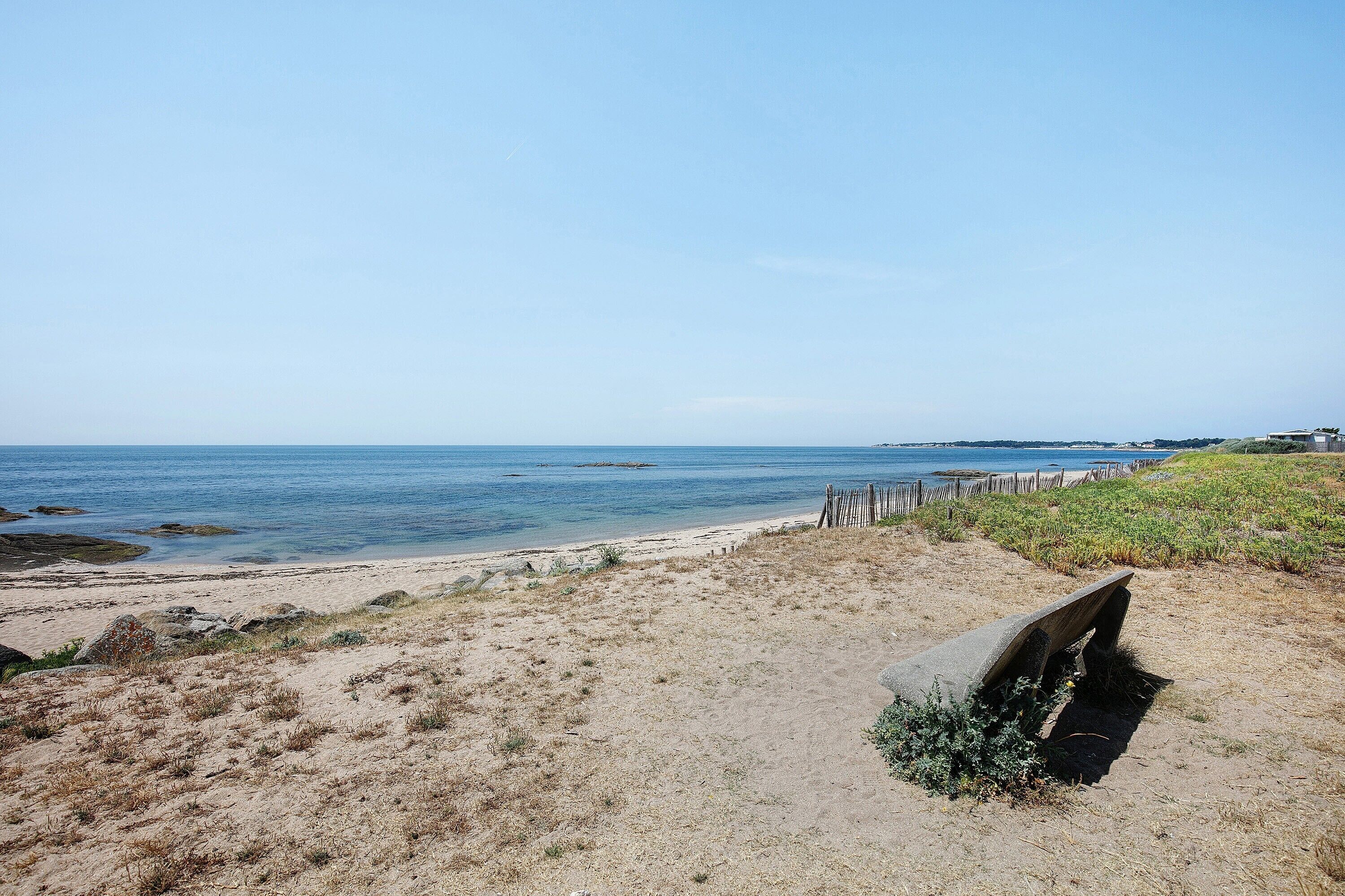 Une plage avec un banc, des dunes de sable et une clôture en bois.