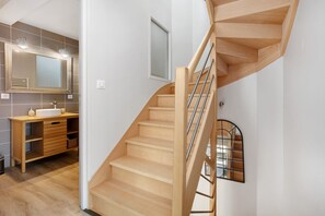 Eine Holztreppe mit Metallgeländer, ein Badezimmer mit Waschbecken und Spiegel sowie ein Fenster mit Aussicht.