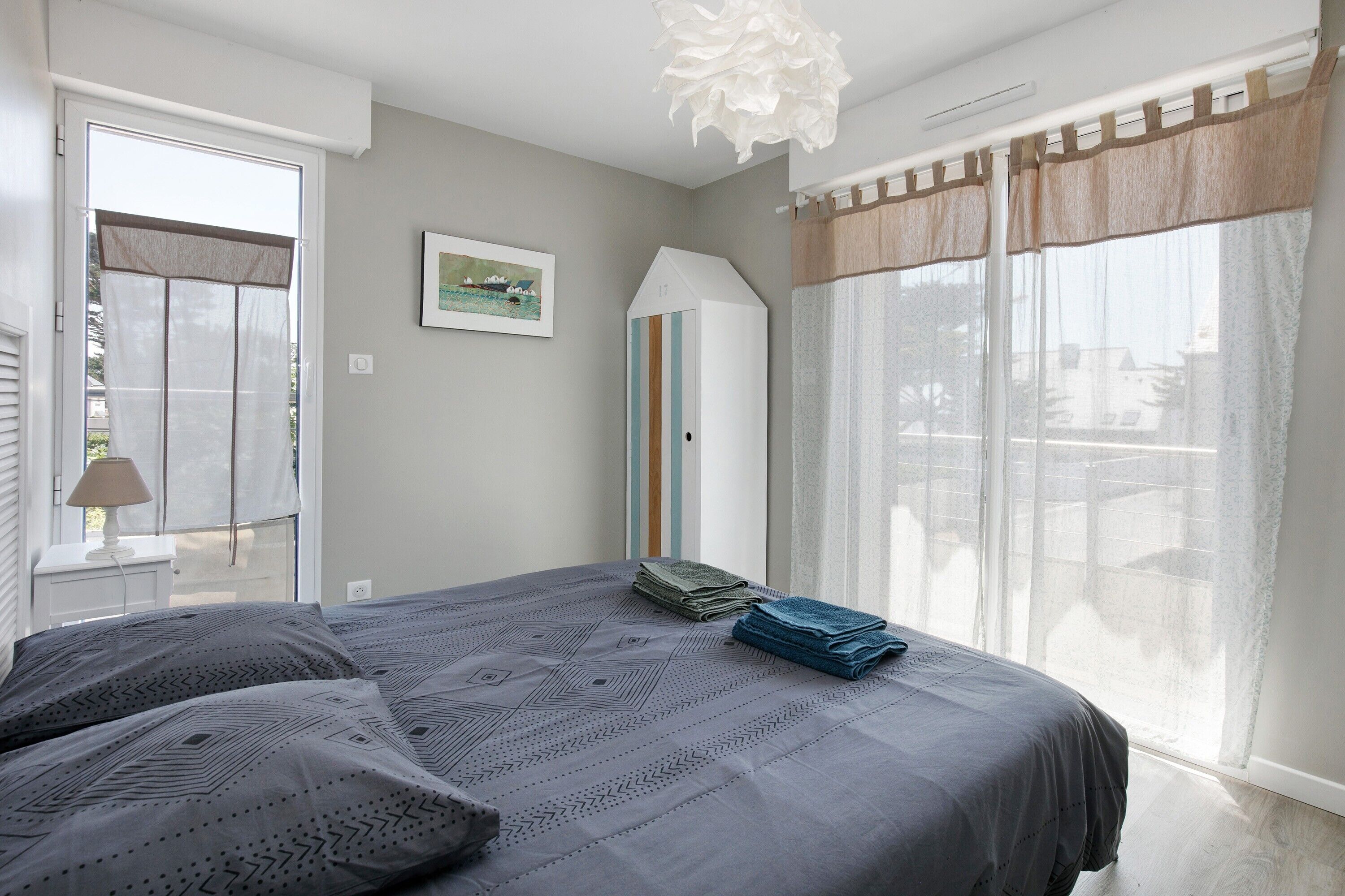 Een slaapkamer met een bed, een raam met gordijnen, een lamp en een lijst met een afbeelding aan de muur.