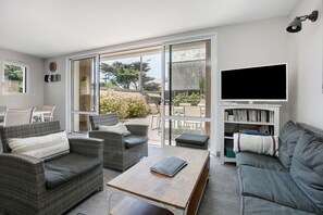 Ein Wohnzimmer mit Rattanmöbeln, einem Flachbildfernseher und einem Bücherregal.