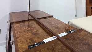 Ein Schlafzimmer mit einem hölzernen Schminktisch, einem Bett, einer Klimaanlage und einem an der Wand befestigten Fernseher.