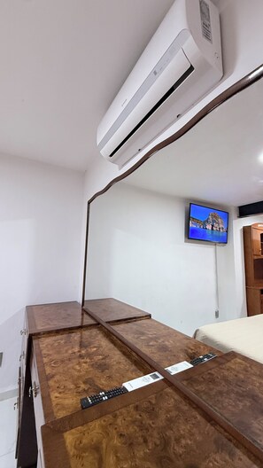 A bedroom with a wooden dresser, a bed, an air conditioner, and a mounted television. - Spacious 4-bedroom apartment in charming Zapopan with AC (Zapopan)