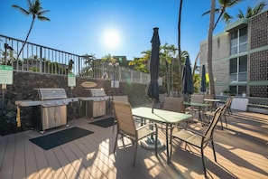 Eine Terrass mit Grill, Sitzgelegenheiten und Blick auf ein Gebäude mit einer Steinmauer.