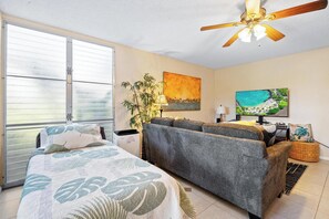 Ein Schlafzimmer mit Bett, Sofa, Deckenventilator, Fernseher und einem Fenster mit Jalousien.