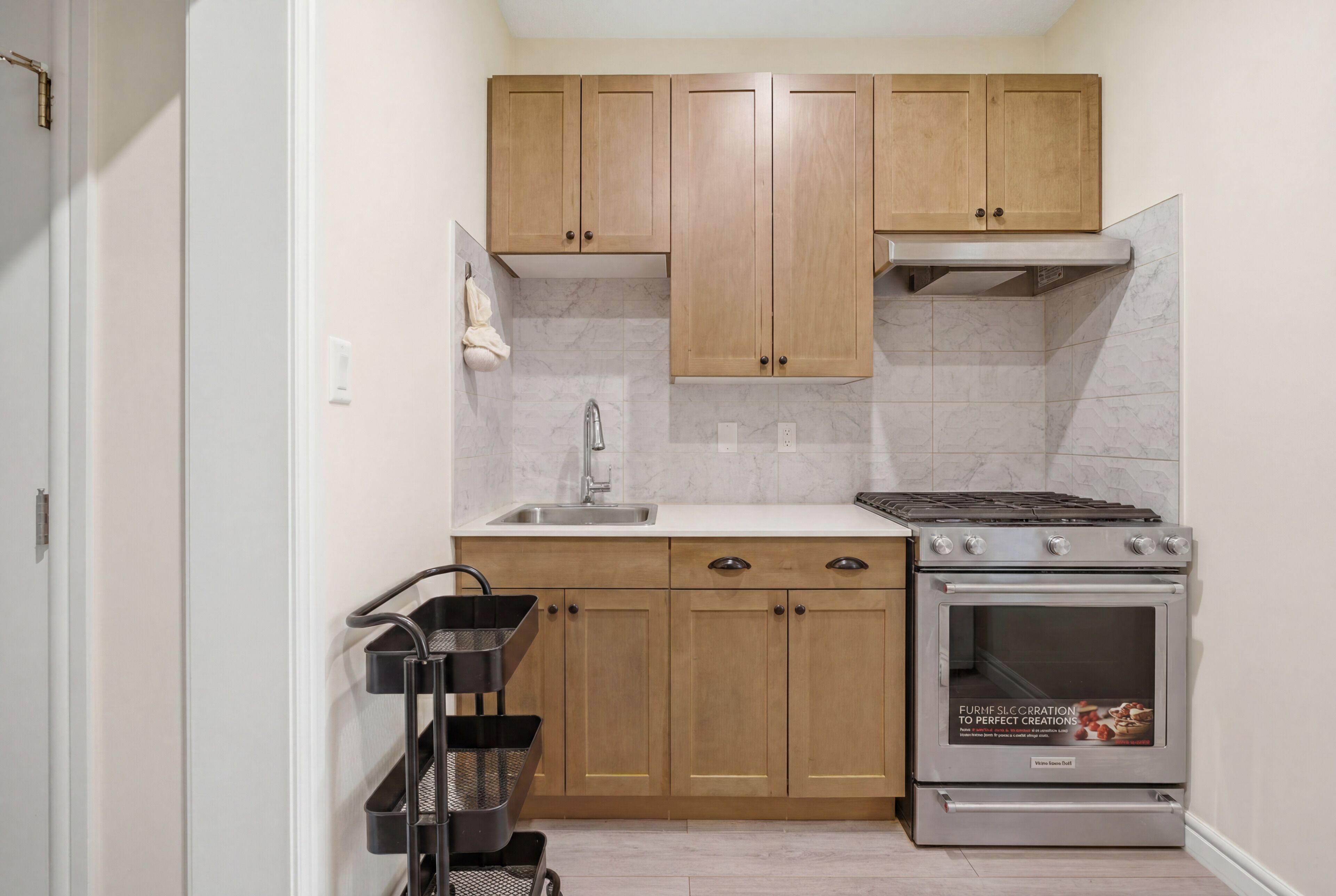 Una cocina compacta con armarios de madera, un lavamanos de acero inoxidable y un horno empotrado.
