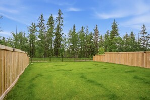 A fenced backyard with a grassy lawn, wooden fence, and tall trees.