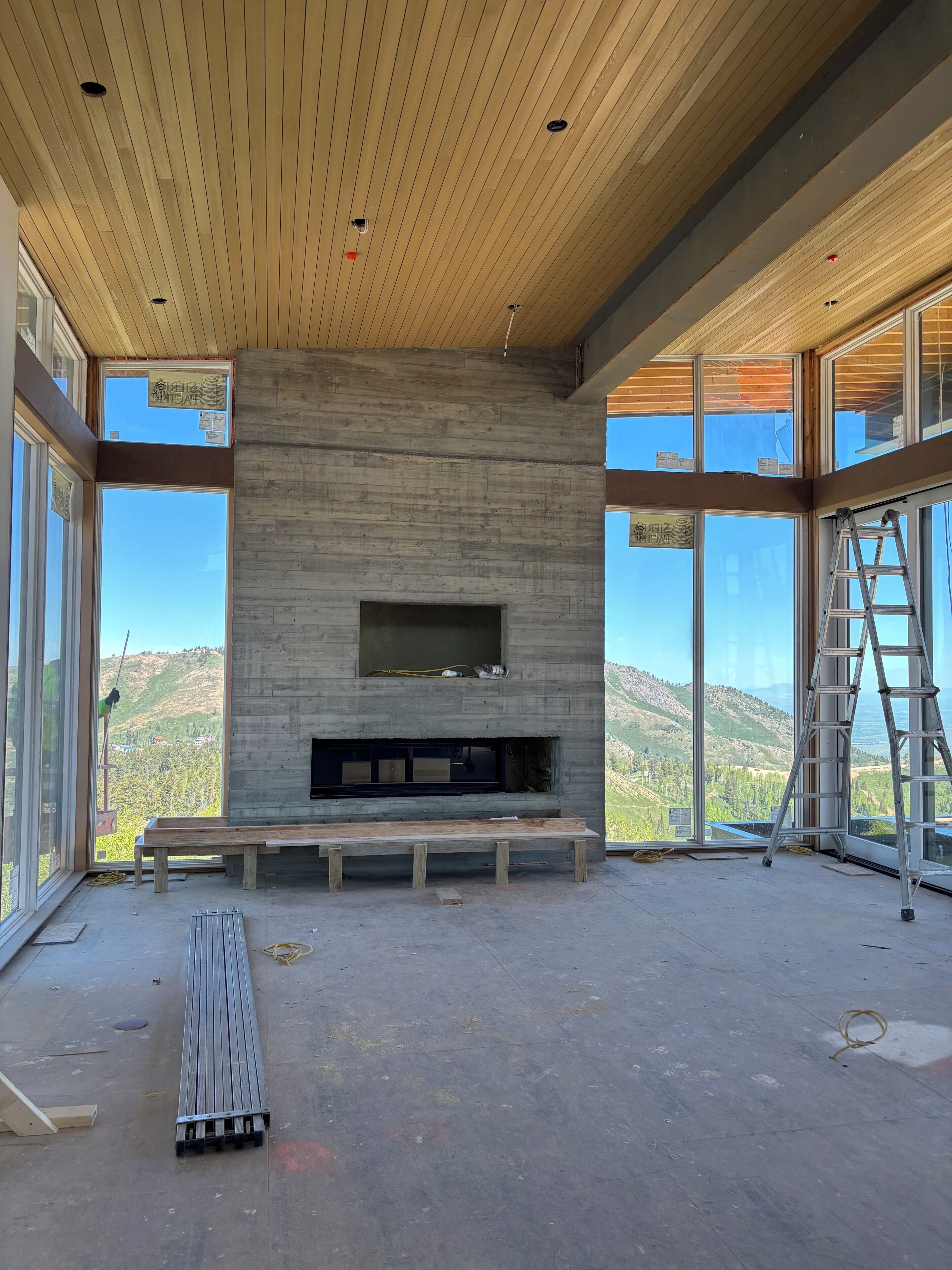 A modern interior with a concrete fireplace, large windows, and a wooden ceiling.