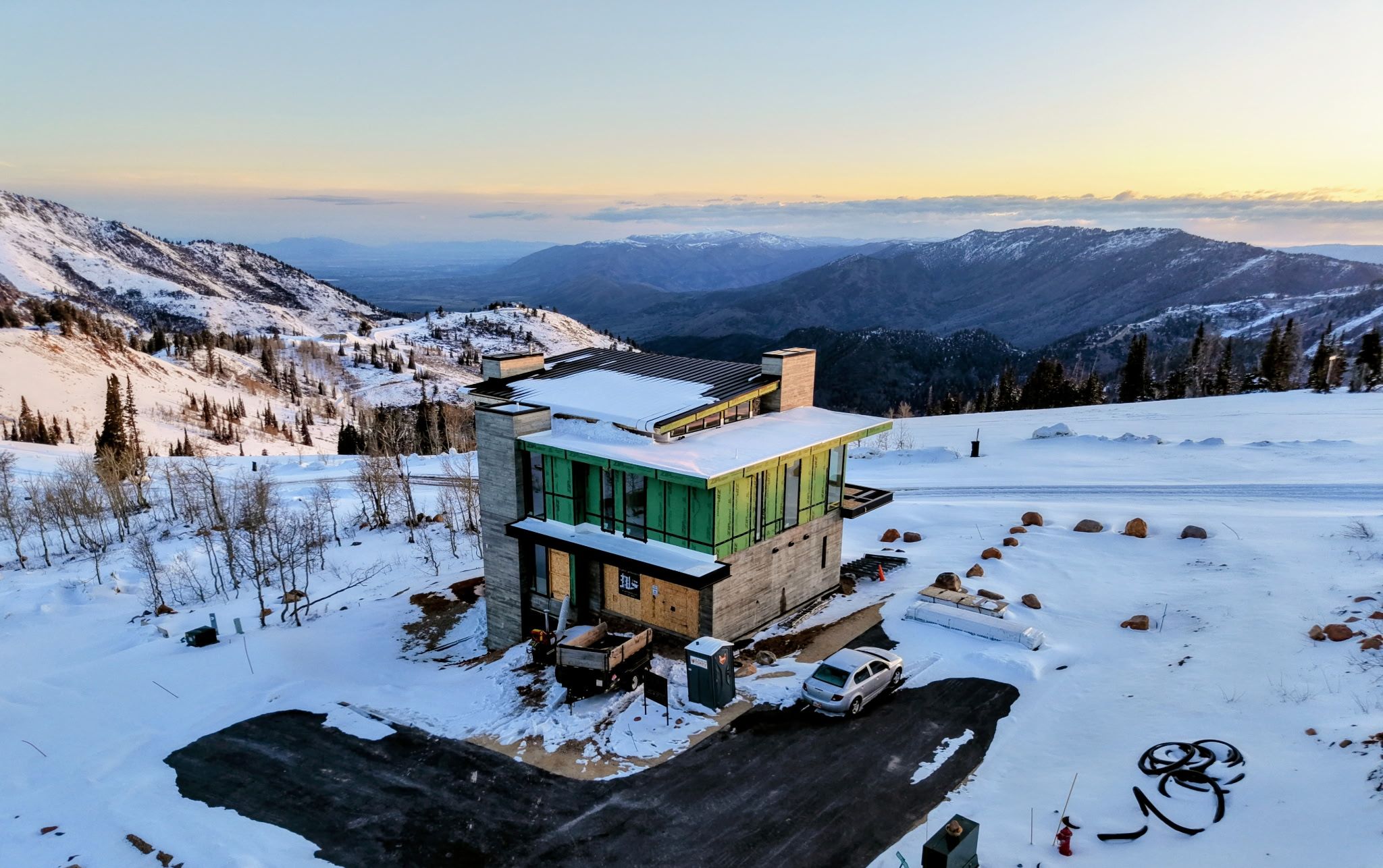 Ett modernt hus med en glasfasad, beläget på en snötäckt bergssluttning med utsikt över avlägsna berg.