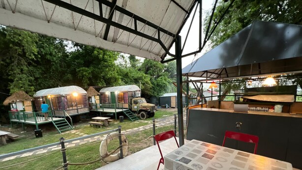 A covered outdoor area with a table and chairs, a thatched-roof structure, and a vehicle. - Ayutthaya Rive Camp And Yacht Charter (Ayutthaya)