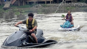 Two people on watercrafts in a body of water with a bridge and buildings in the background. - Ayutthaya Rive Camp And Yacht Charter (Ayutthaya)