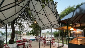 An outdoor dining area with tables and chairs, a covered seating area, and a view of a river. - Ayutthaya Rive Camp And Yacht Charter (Ayutthaya)