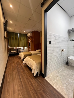 A hotel room with a wooden floor, two beds, a small desk, and a bathroom with white tiles. - Hotel De Venne (Genk)