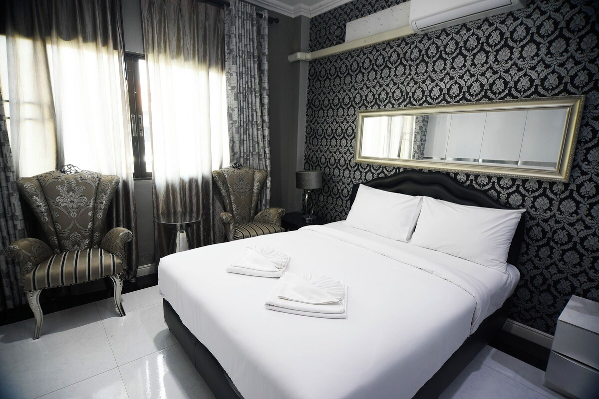 Een hotelkamer met een groot bed, twee fauteuils, een nachtkastje en een spiegel.
