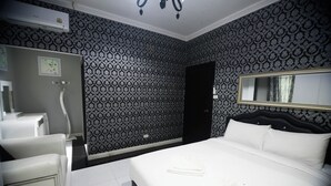 Camera d'albergo con carta da parati a motivi, un letto con lenzuola bianche, un comodino, uno specchio e un box doccia.