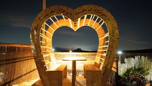 A heart-shaped structure with text, a table, and benches in a desert setting.