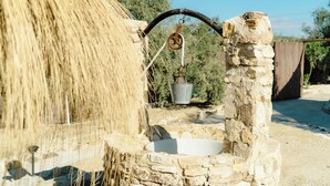 A stone well with a rope and pulley system, surrounded by dry grass and a rustic fence.