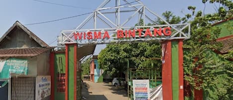 Um portão de metal com a inscrição 'WISMA BINTANG' acima, dando acesso a um caminho.