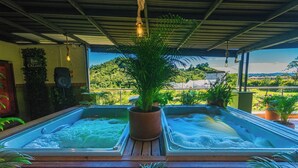 Ofurô com deck de madeira, cercado por plantas em vasos e vista para uma paisagem verde.