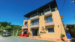 Um edifício de dois andares com varandas, uma placa com a inscrição 'Bambú HOTEL' e área de estar externa.