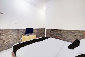 Quarto com uma cama, cômoda e televisão em parede de madeira.