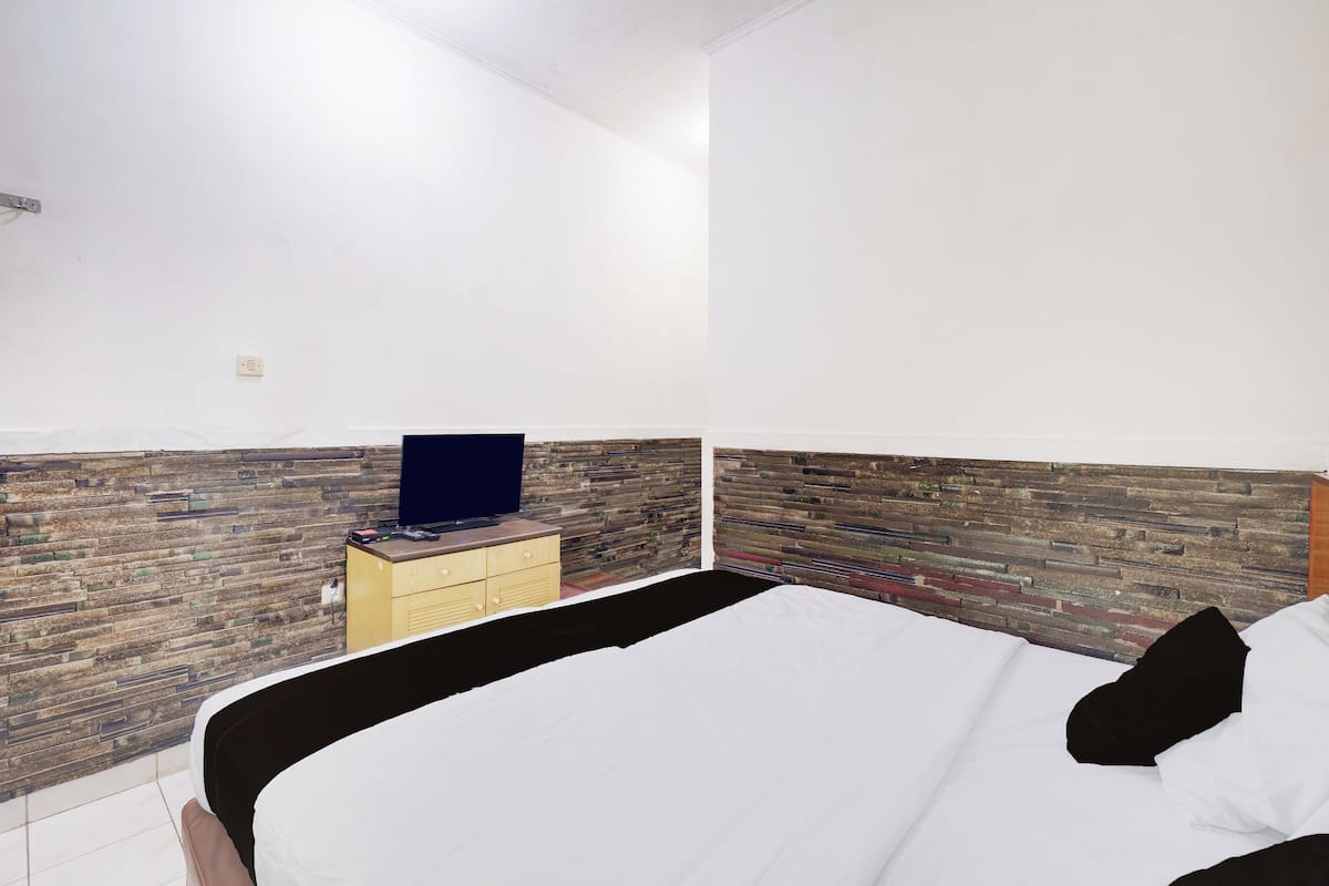 A bedroom with a bed, a dresser, and a television on a wooden wall.