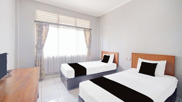 A hotel room with two beds, a wooden desk, and a window with curtains. - Hotel O Bogor Near Taman Safari (Cisarua)