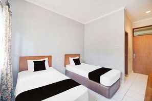Habitación de hotel con dos camas individuales, una puerta de madera y suelo de baldosas.