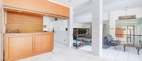Un área de recepción con un mostrador de madera, una escalera con barandilla de metal y una zona de estar con una silla.